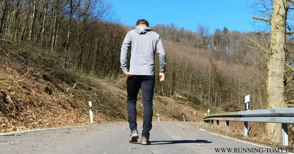 Läufer von hinten geht eine asphaltierte Straße entlang.